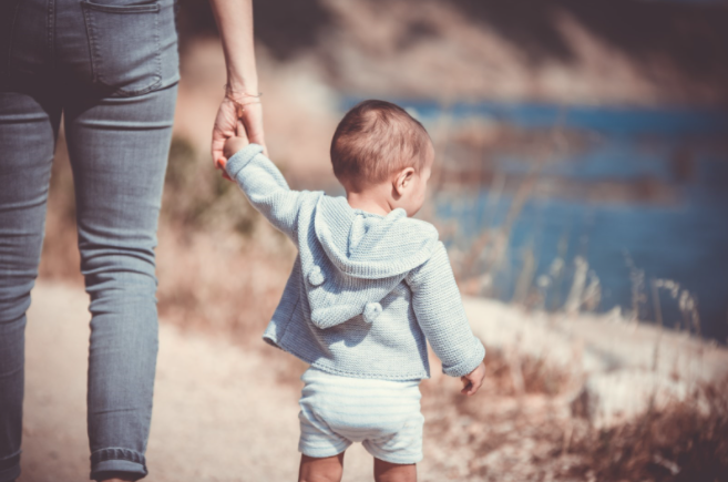 Image of child holding hands with a parent in the sun