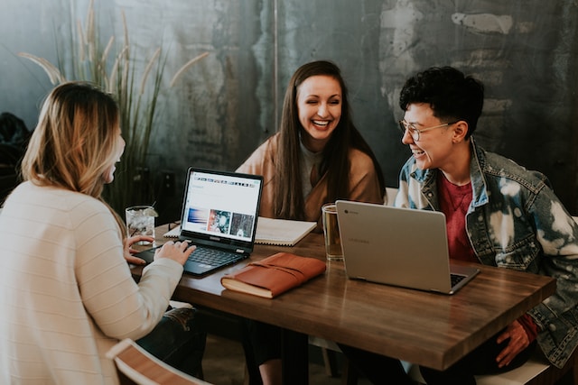 3 young people sitting around a table with computers